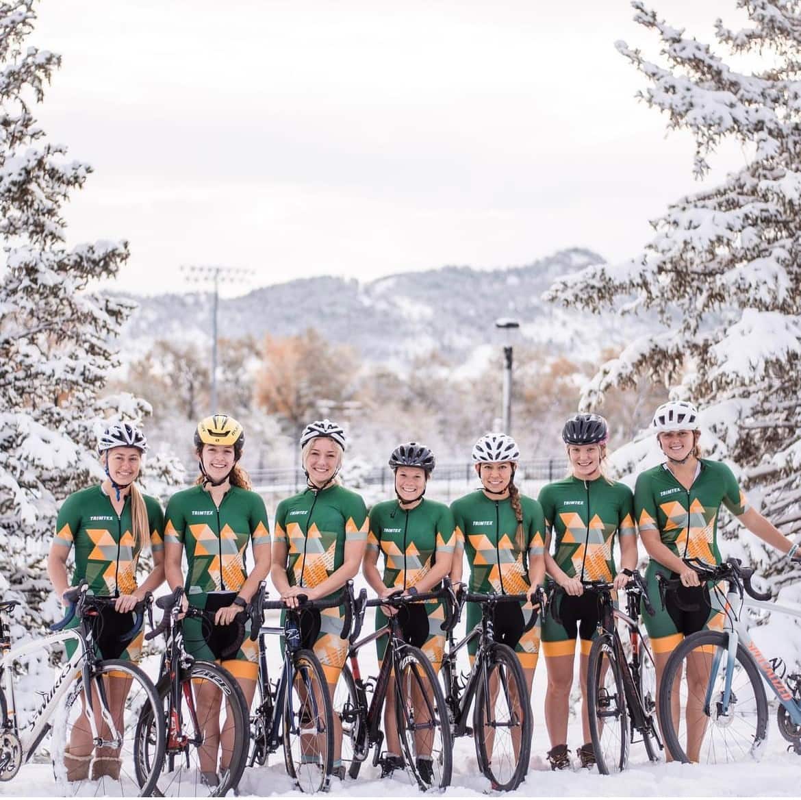 women's collegiate triathlon team posing for a photo holding their bikes while standing in the snow