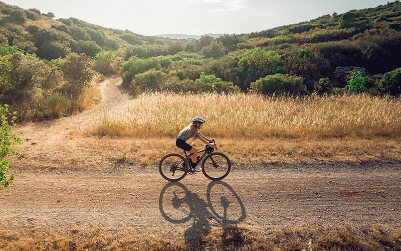 woman riding a gravel bicycle on a dirt road in a scenic area with golden light