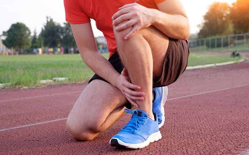 An athlete holds their knee and shin as if they are experiencing leg pain.