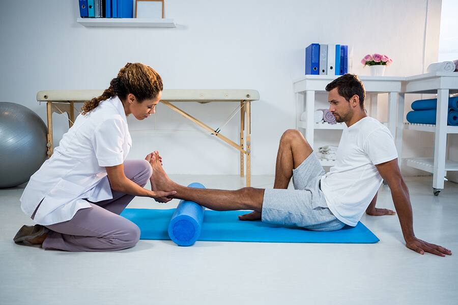 A physical therapist helps a patient use a foam roller on his calf.