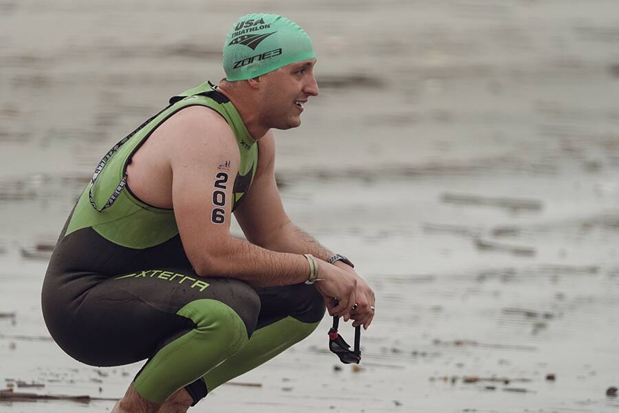 A tritahlete squats on the beach before entering the water prior to the swim portion of a race.