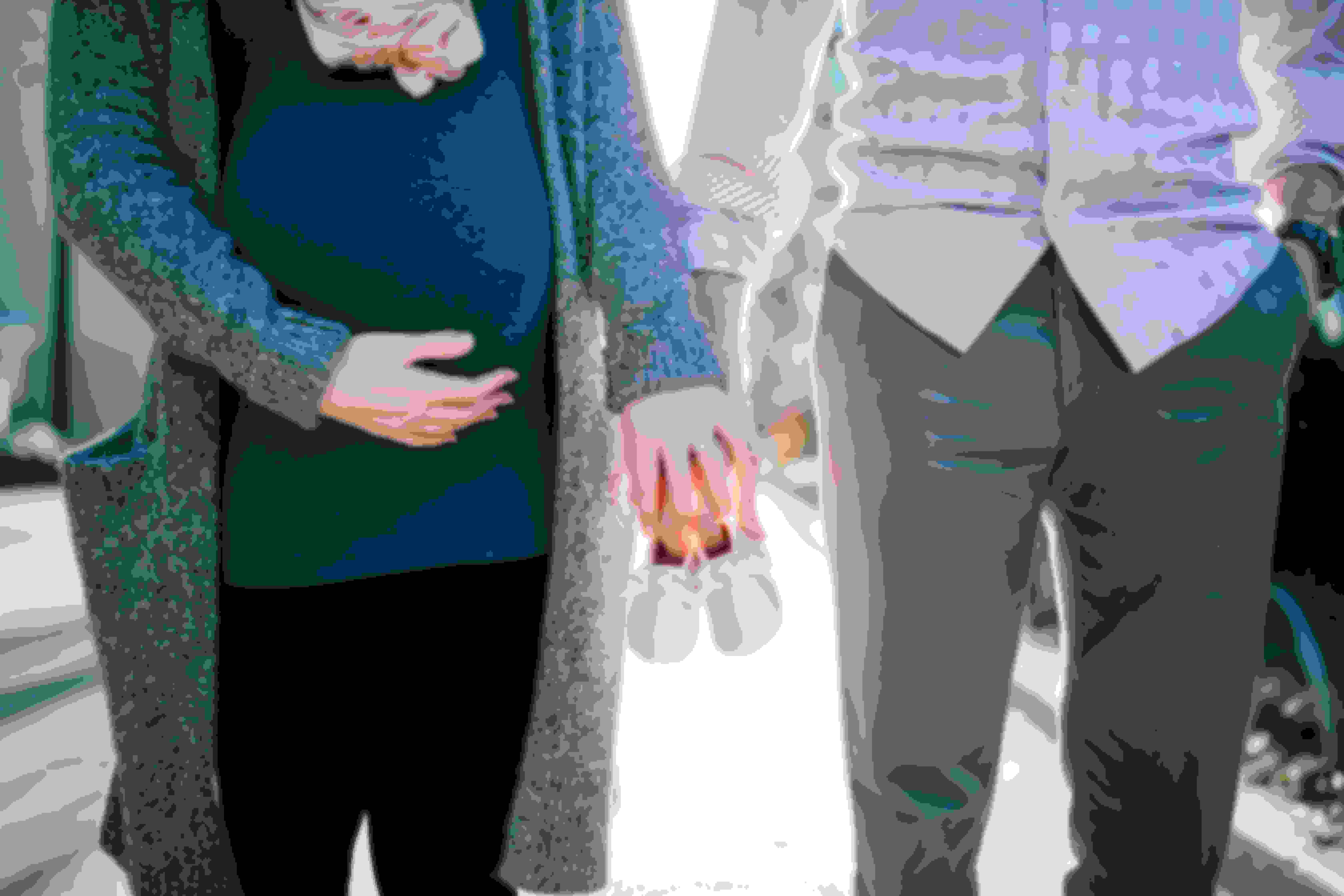 Couple comprising of a man and a pregnant woman holding hands with baby shoes on their hands