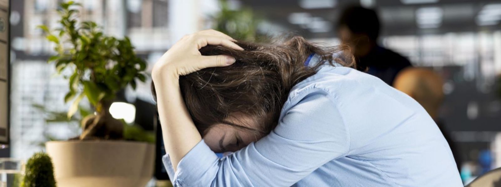 nő egy irodában ül, láthatóan fáradt és gondterhelt, a lelki fáradtság jeleit mutatja