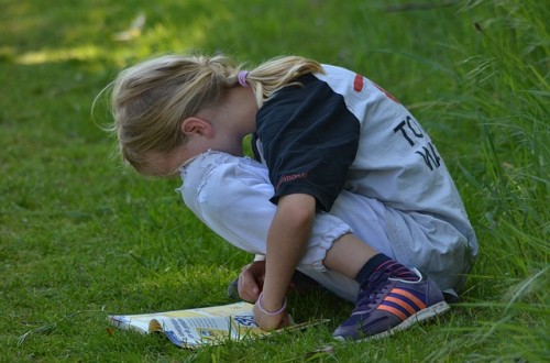 Criança com TDA lendo uma revista no gramado.