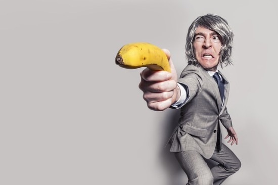 Homem de negócios de terno cinza apontando a direção com uma banana na mão.
