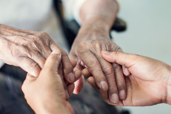 Hände von Seniorin in Rollstuhl werden gehalten von jungen Händen