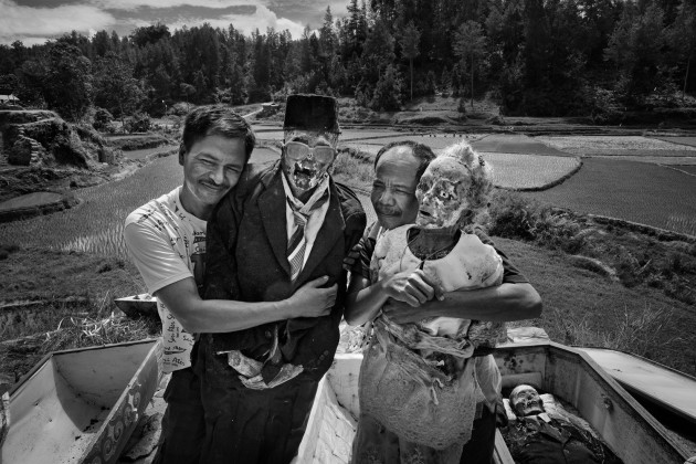 © Alain Schroeder, Belgium. WINNER, TRAVEL PHOTOGRAPHER OF THE YEAR 2017. Dumbia village, Pangala, Toraja, Sulawesi Island, Indonesia. Ma' Nene ceremony. Brothers Micha from Jakarta and Misi from Makassar embrace their parents, father Tumaang and mother Rara. The grave house is located on top of a hill overlooking the rice fields.