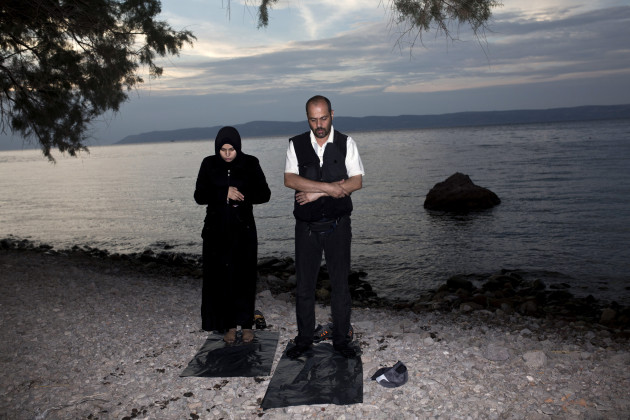 GREECE, LESBOS : Migrants pray after arriving on the shores of the Greek island of Lesbos aboard an inflatable dinghy across the Aegean Sea from from Turkey on September 9, 2015. Overwhelmed by the 20,000 refugees and migrants currently camped on the holiday island, authorities hastily set up a refugee registration centre September 8 on a parched old football pitch. Local authorities have found it impossible to keep up with the pace of the influx, and tensions have boiled over. AFP PHOTO/Angelos Tzortzinis