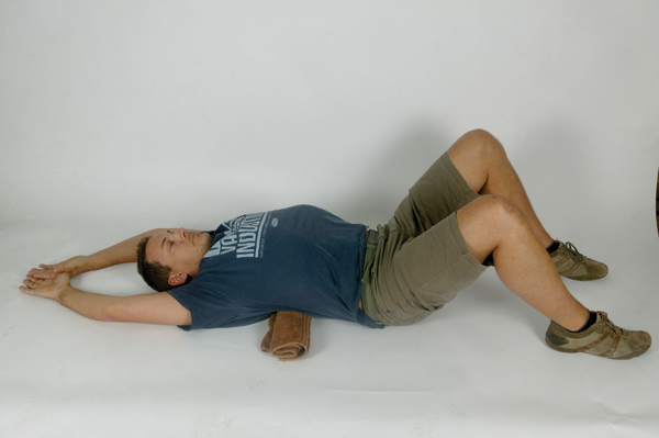 Okay, dropping to the ground underneath your desk may not be viable at the office, but this is a nice passive stretch that shouldn’t be too much of an imposition before bed. It is hard to get your head on top of your shoulders, and keep your shoulders back, unless you have good mid-back mobility. This stretch should be a pleasure after a long day tapping the keys (and also after a long day in the saddle for those lucky enough to get out!)
Lay on your back, hips and knees bent, feet on the floor. Have rolled up towel placed crossways underneath your back, in the mid-back (thoracic) area. Lift your arms above your head to rest on the floor. Hold 20 seconds, then repeat with towel in a slightly higher position. Do this one at the end of every day.