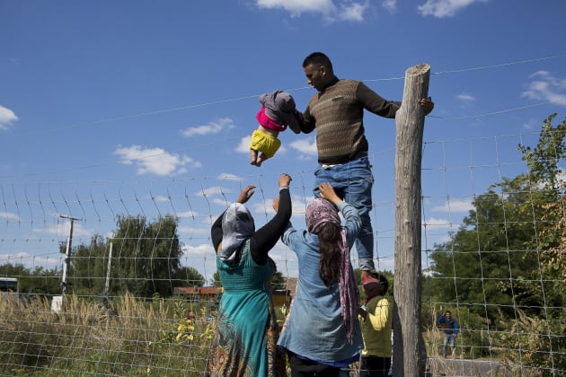 A man lifts an infant over a fence running along the M5 motorway in Serbia. Approx. 200 migrants, marched out of a temporary camp stationed at the border of Hungary and Serbia and were met with riot police with dogs. 9 September 2015, Röszke, Hungary. © David Maurice Smith/Oculi.