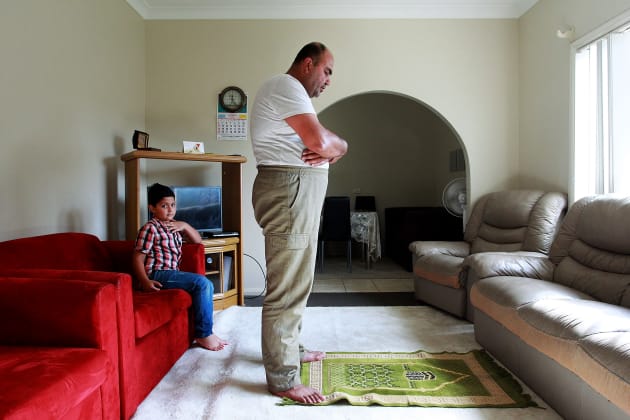 Ahmad looks on as his father Abdullah Tinawi prays in their living room on 16 December, 2015 in Wollongong. The Tinawi family from Al-Zabadani, southwestern Syria have found refuge in Australia following a long and tumultuous journey from their homeland in 2012. © Lisa Maree Williams.