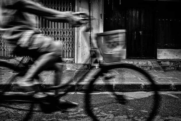 Cyclist riding his bicycle down the street in Yangon City, Myanmar. I anticpated the moment he would pass through my frame while using a slow shutter to add a slight sense of motion blur. Fujifilm X100S, 23mm lens @ 23mm, 1/20s @ f5.6, ISO 400, handheld. Contrast, curves and levels adjustment, sharpening and monochrome conversion in Photoshop CC. Photo © Drew Hopper.