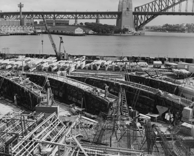 This high angle view of the casting yard shows the concrete segments for the roof of the Sydney Opera House. Danish architect Jorn Utzon won an international design competition to design the building. This image is originally from the analogue files of the Fox Photos news agency which, though based in London, covered world events. The print may have not made it to wide circulation at the time it was taken but is now published online for the first time and gives us an early glimpse as the mammoth project began.