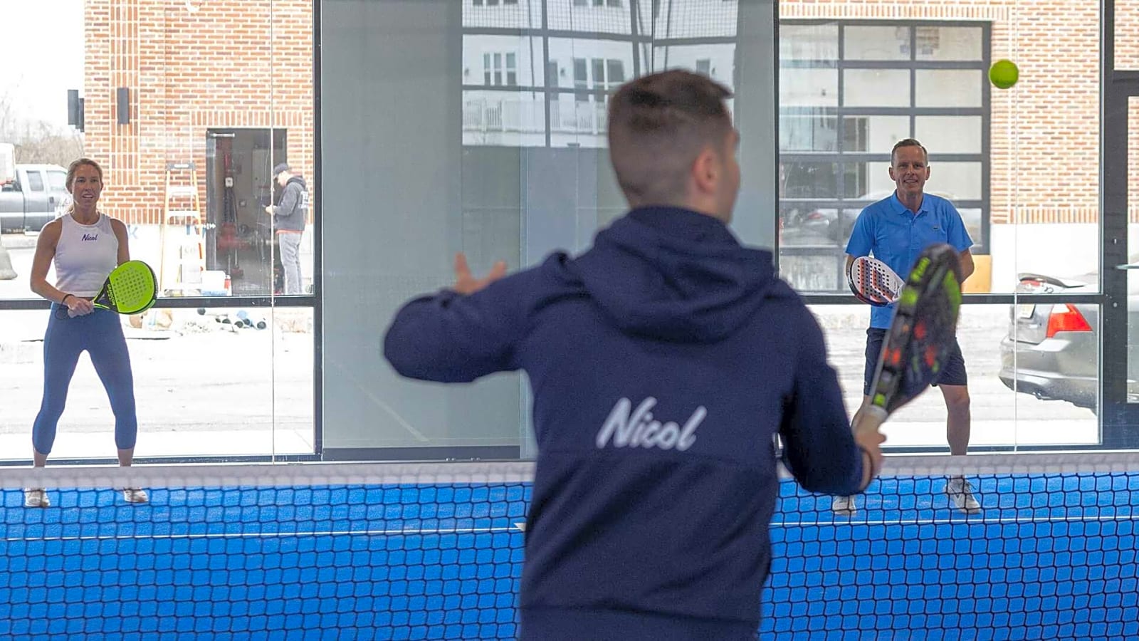 Rodrigo Magalhaes hits a padel ball back towards Peter and Jess Nicol