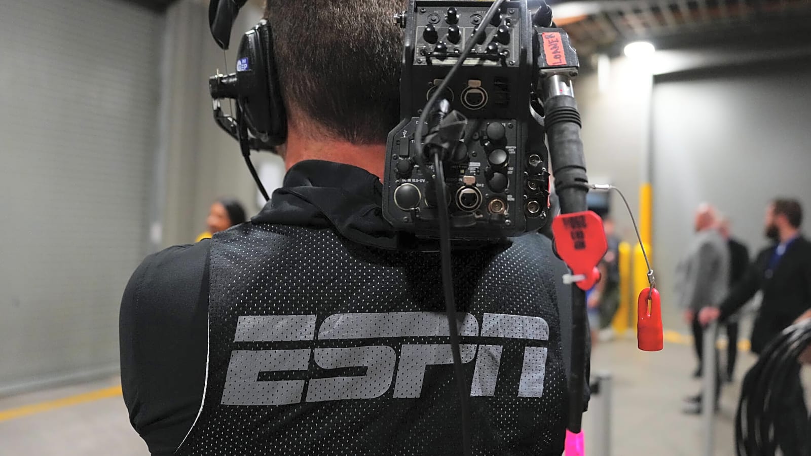 An ESPN Boradcaster Facing Away From The Camera With ESPN Written On The Back Of His Press Vest