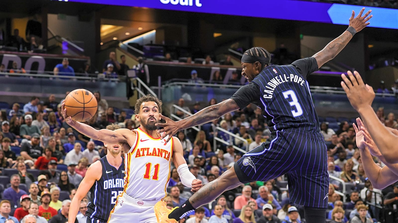 Point guard Trae Young in motion as he passes around outstretched Kentavious Caldwell-Pope in Orlando, Florida in the early-April Hawks vs. Magic showdown