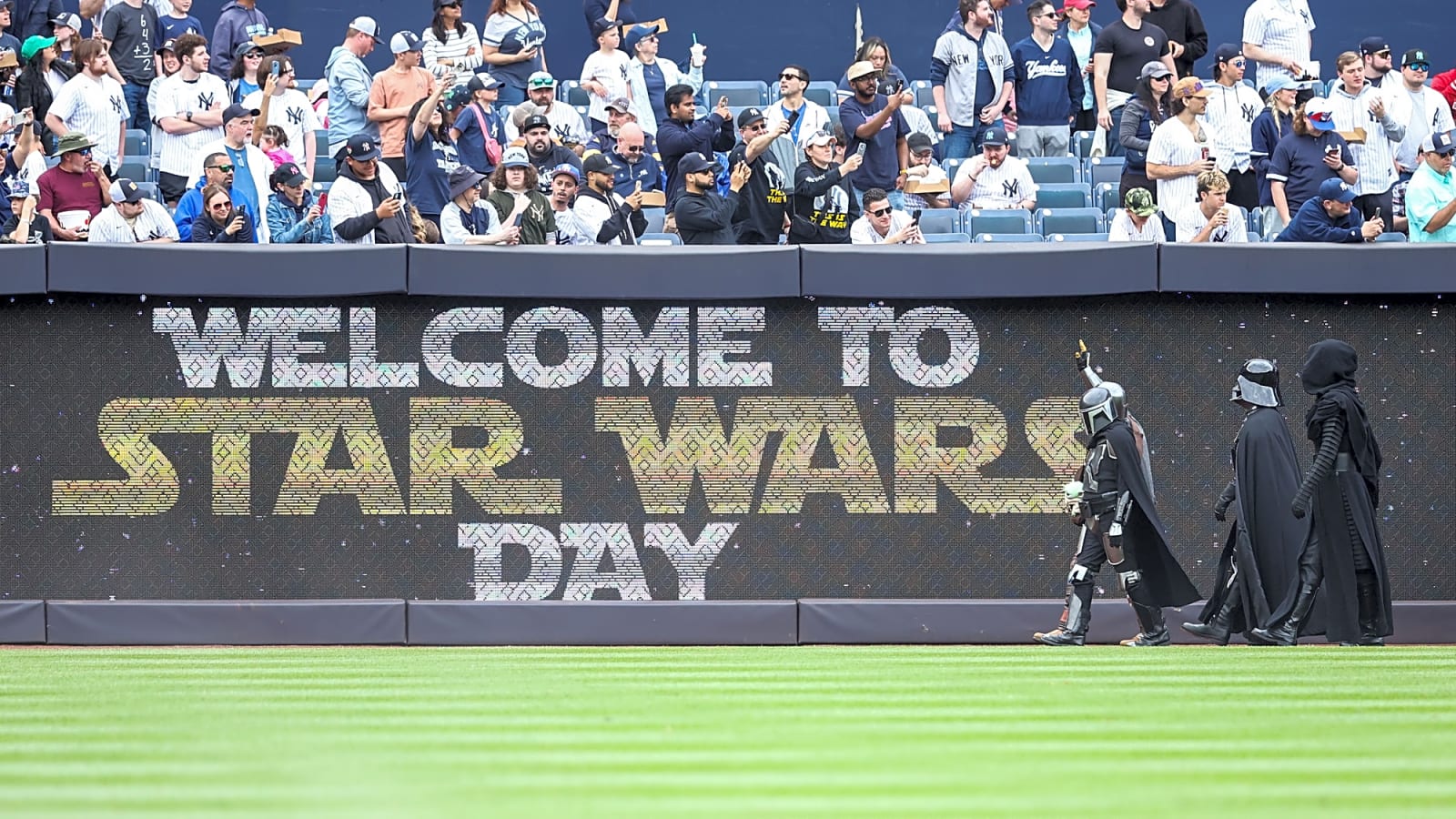 A troop of Sith-dressed character march in front of sign "Welcome To Star Wars Day" for a May the 4th promotion at Yankee Stadium