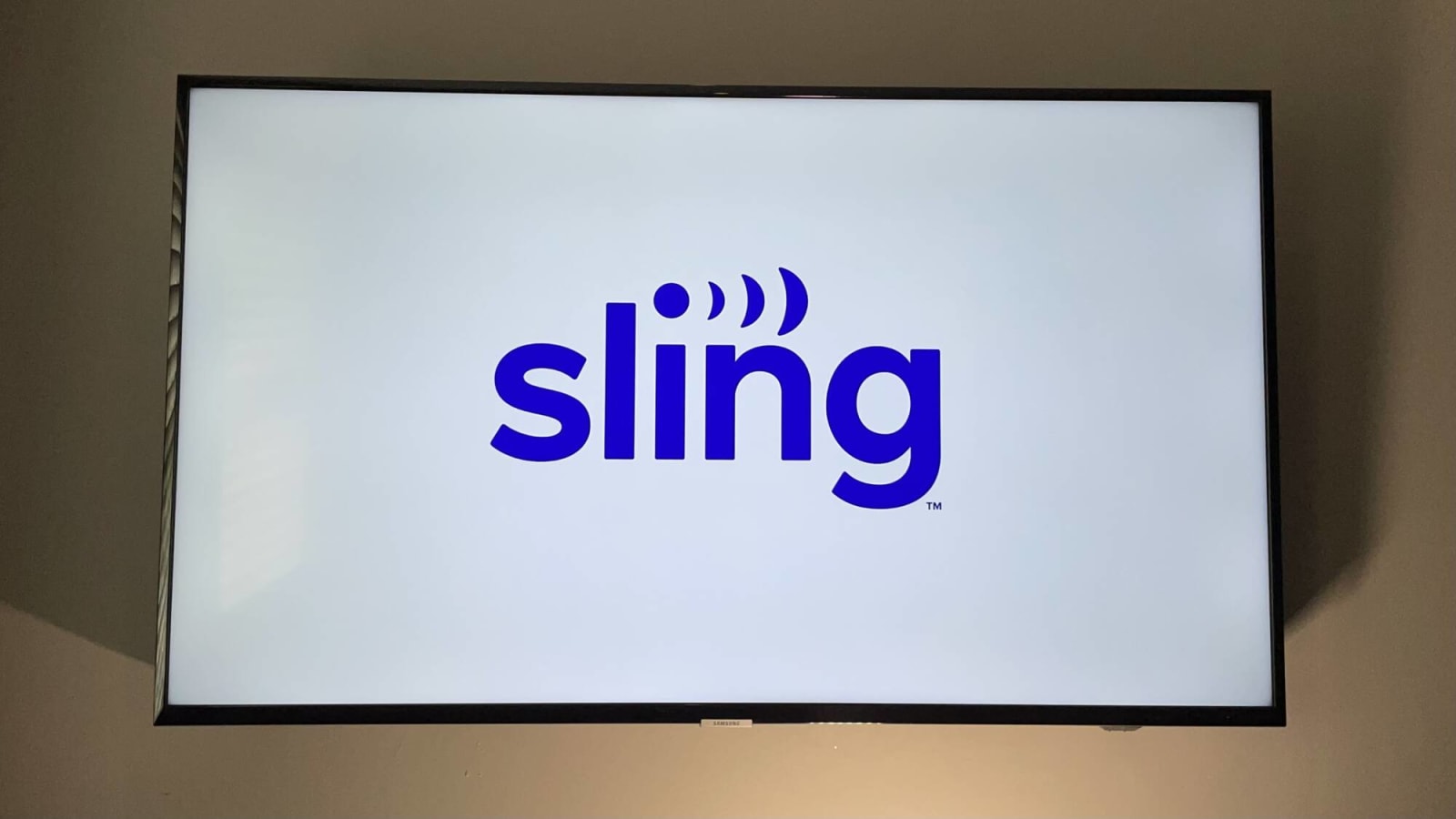Sling TV logo in blue against a white background on a mounted TV in a living room