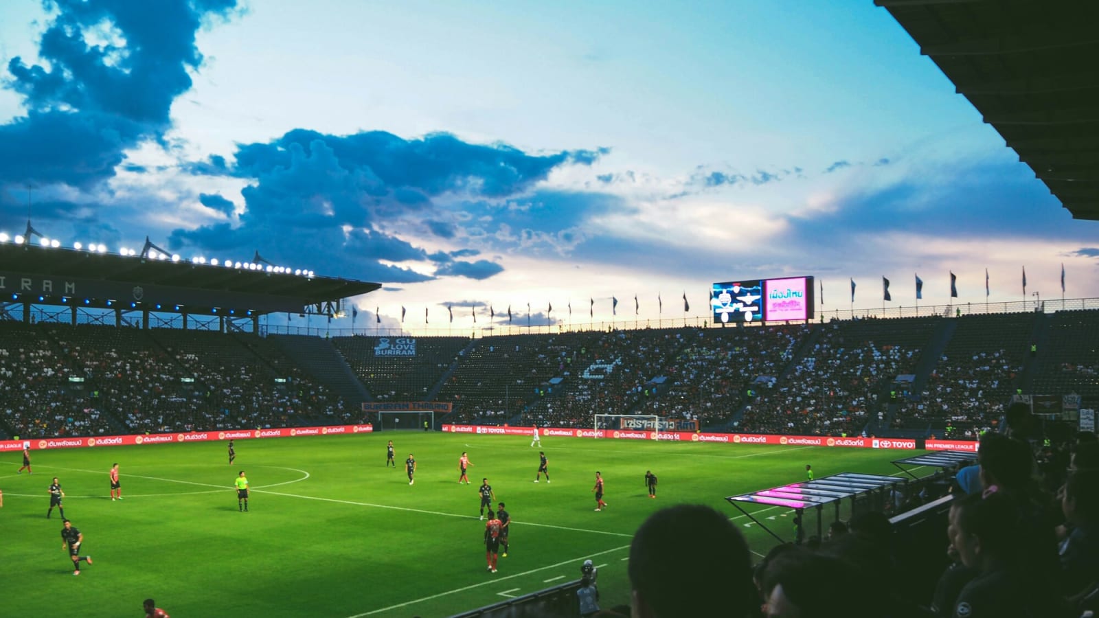 Fans watching a soccer game in an arena in the evening with a slightly cloudy sunset