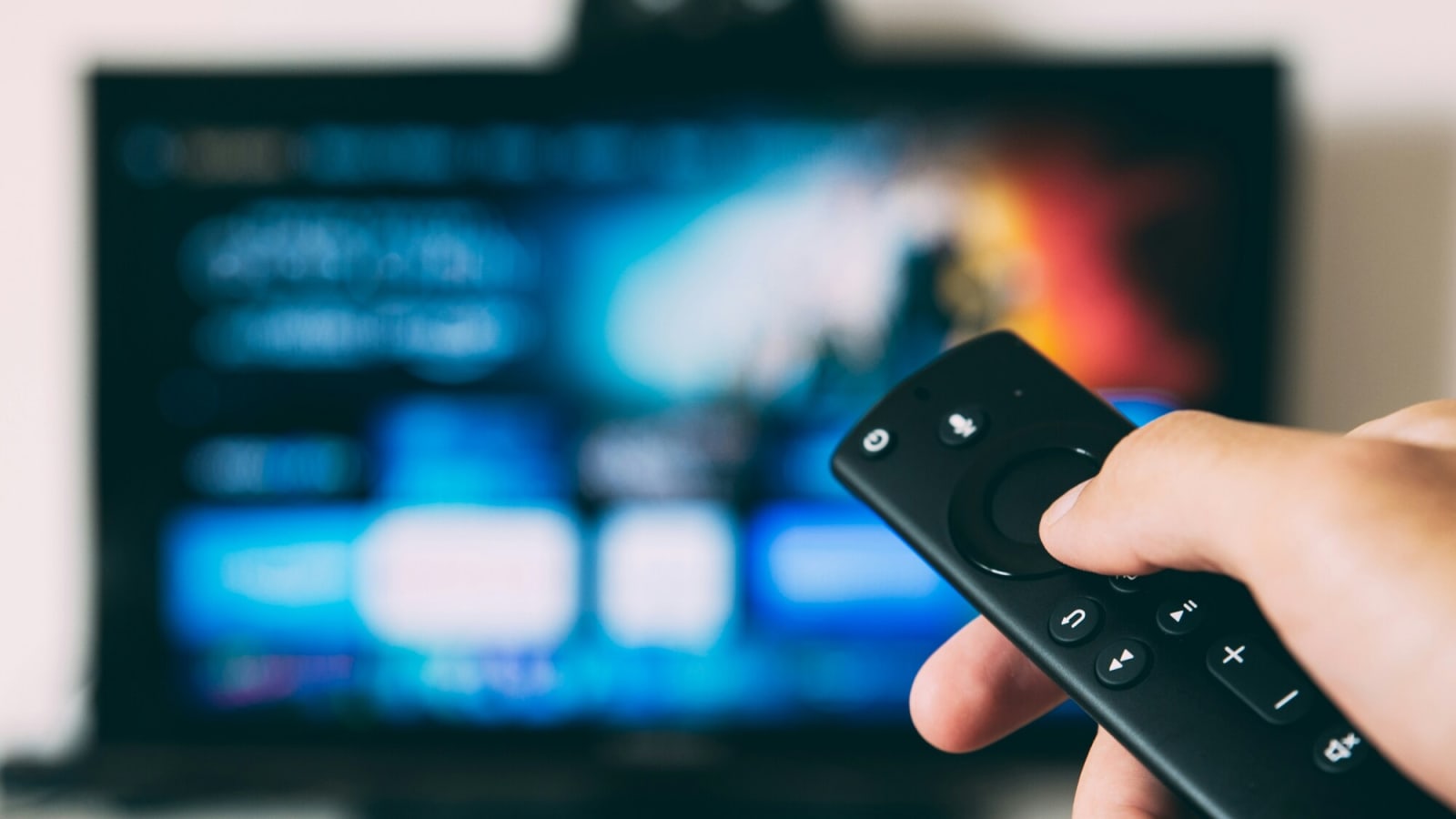 Blurred Flat Screen TV in background with smart remote being held by a hand