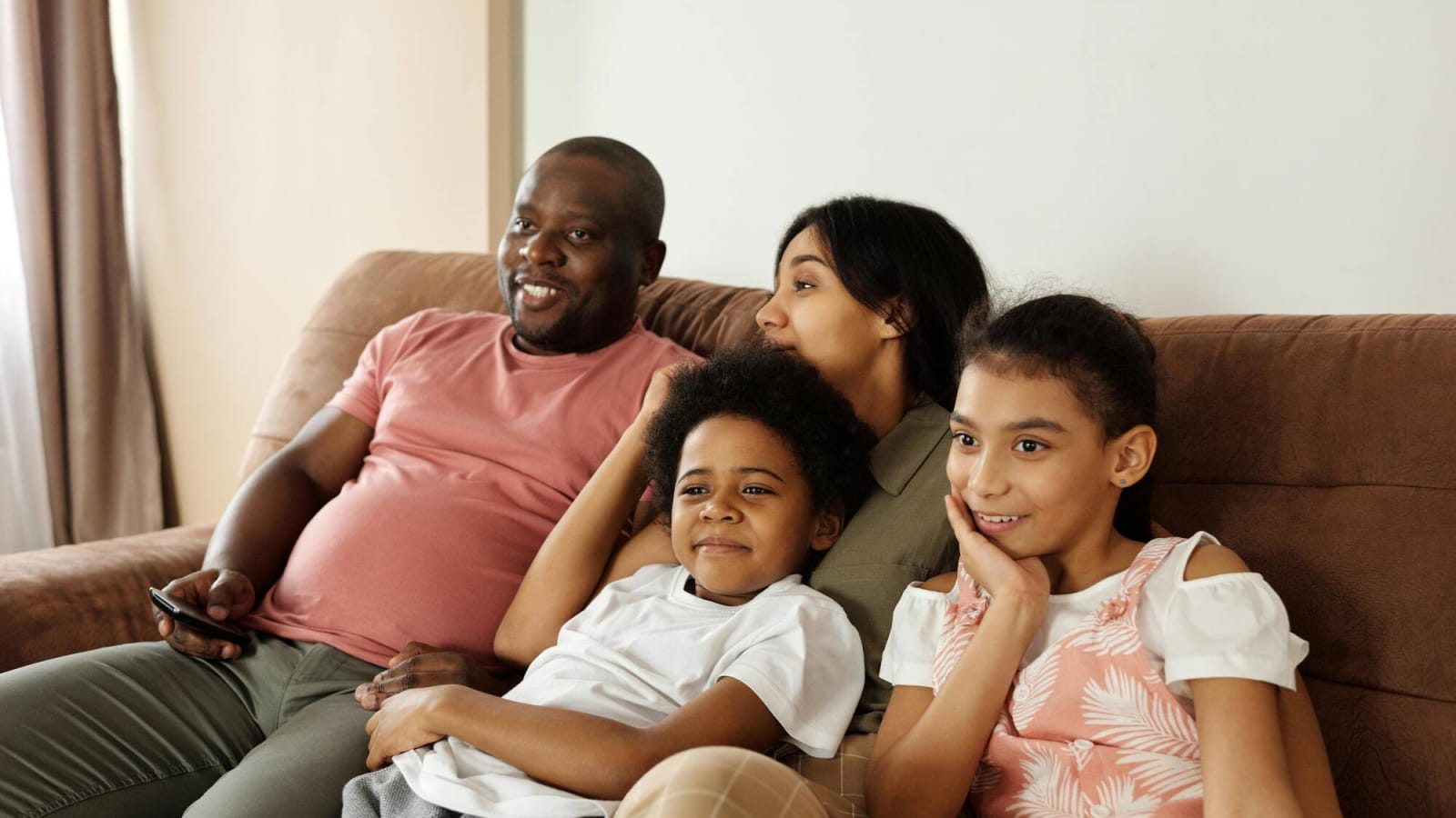 A happy family sitting on the couch and watching TV while the father holds the remote in his hand