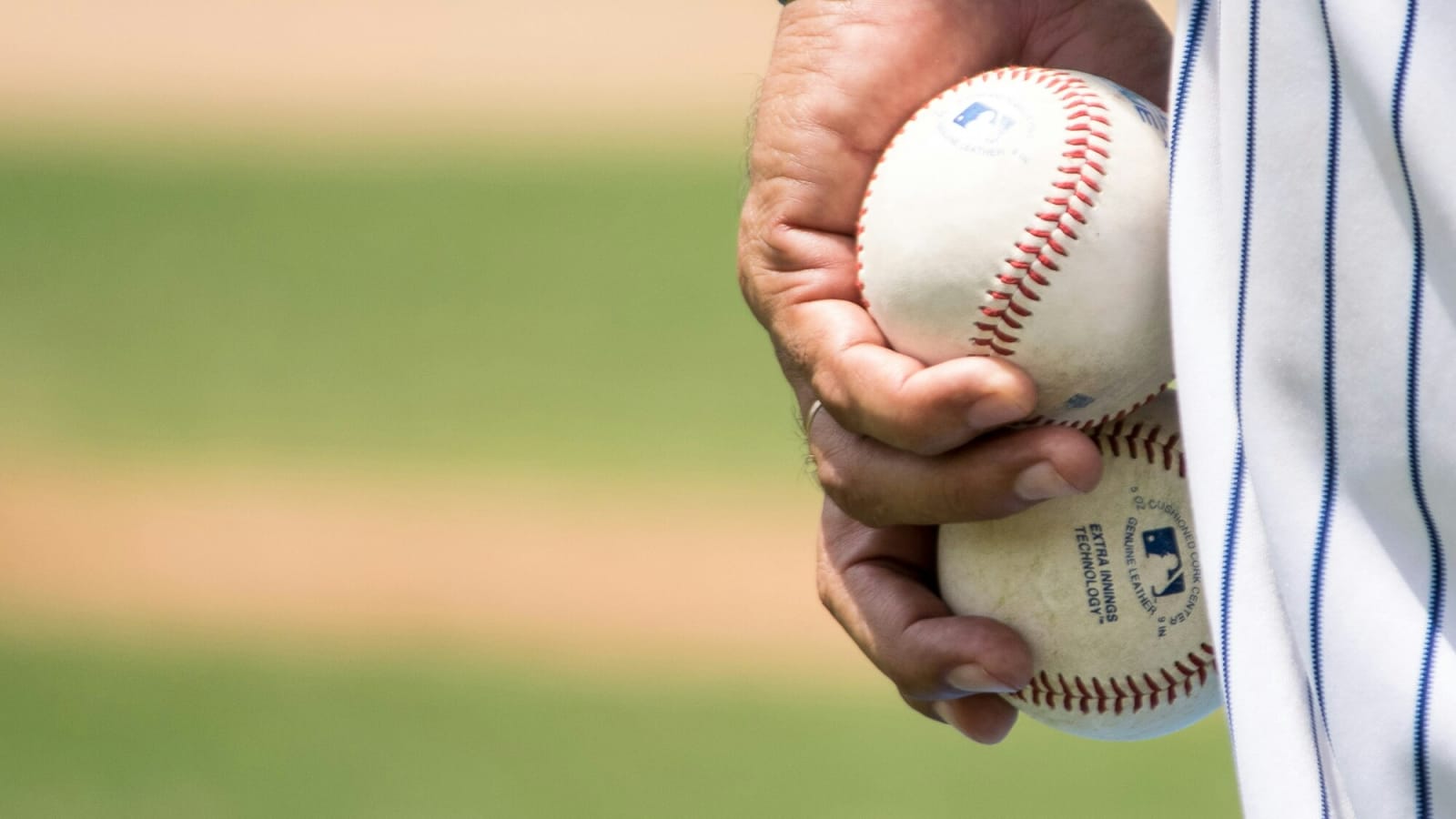 Player holding two baseballs in hand with blurred field in background
