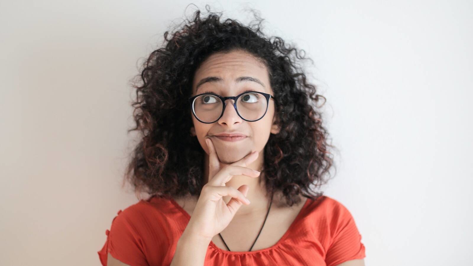 Woman wearing eyeglasses making a thoughtful face against white wall