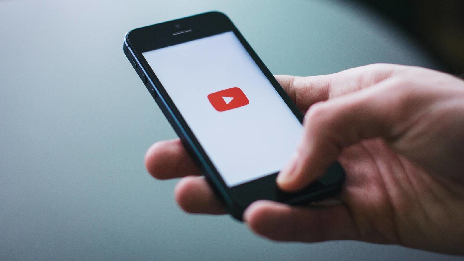 Hand holding a black phone showing the YouTube TV logo on a white background
