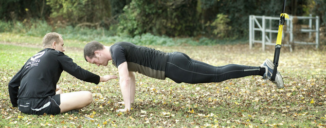 personal trainer using trx for core doing plank in a park