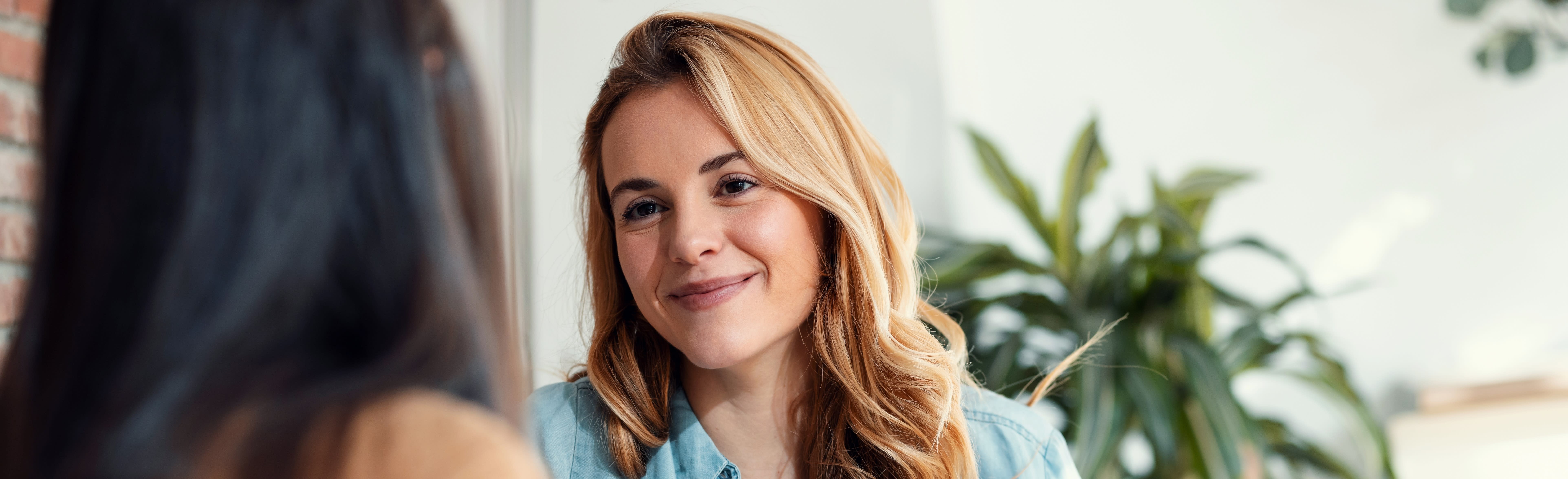 A woman holding a glass of red wine, making a cheers motion to her friend.