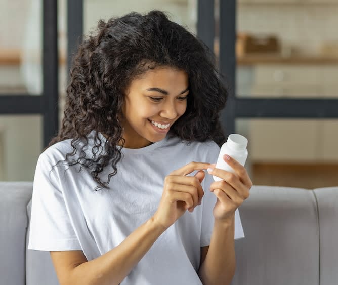A pair of women's hands, wearing a gold ring, opening a Cove medication bottle.
