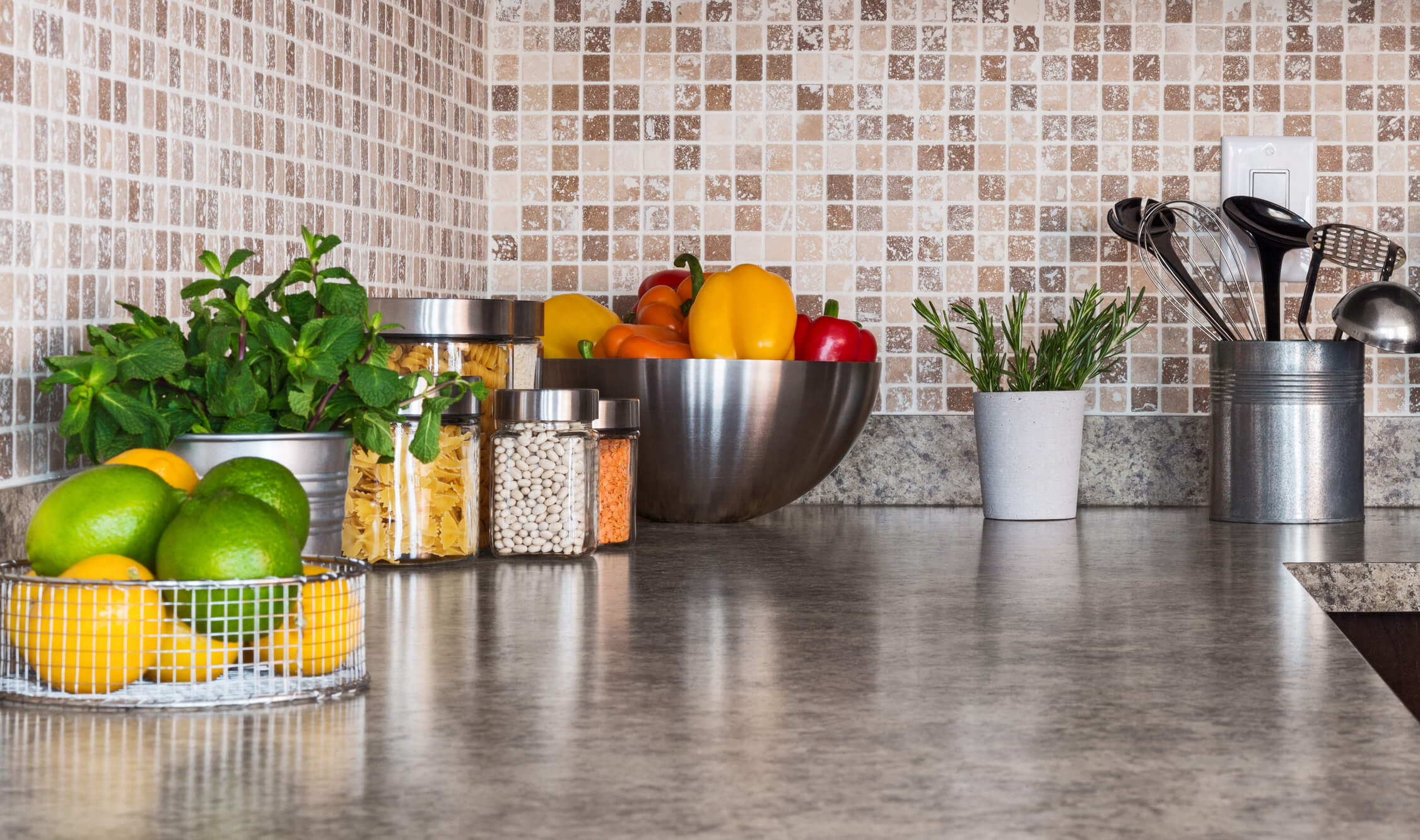 A clean kitchen counter with bowls of fruit and jars of dried goods on top