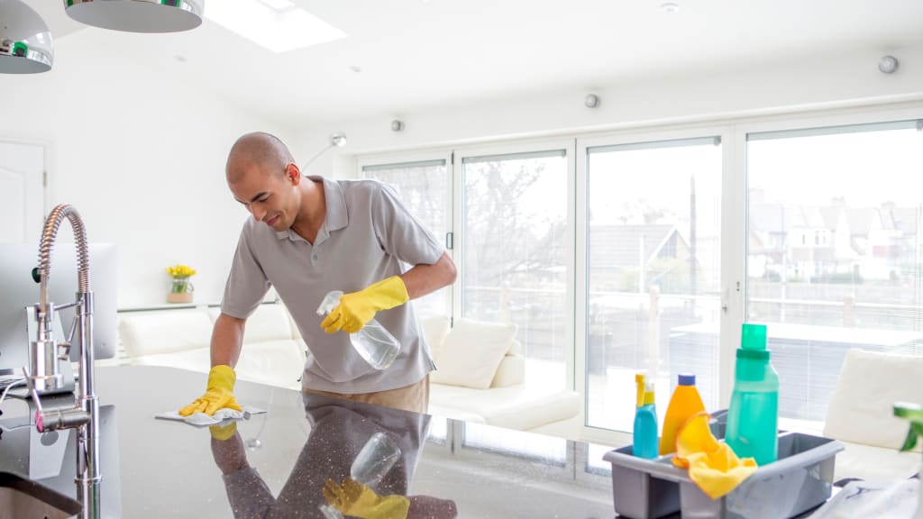 A man cleans a counter while tackling his Spring Cleaning List in the Kitchen