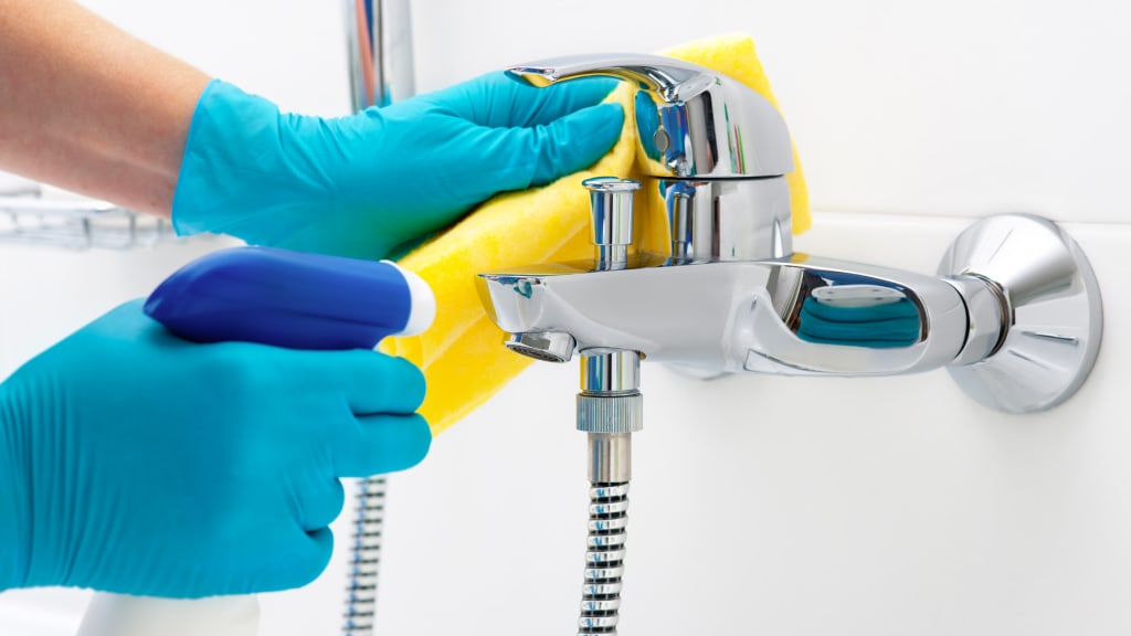 Two gloved hands wiping a bathtub faucet as part of deep house cleaning services.