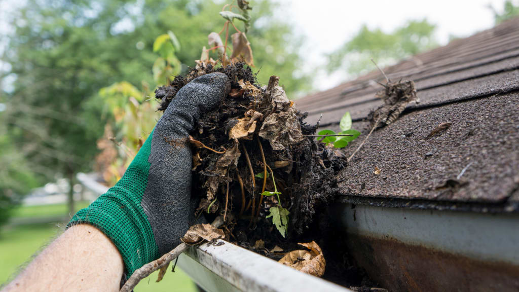 A hand wearing a glove cleans leaves out of a gutter, part of winter home prep tasks.