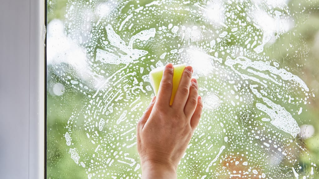 a hand wipes soapy water on a window with a sponge while using spring cleaning hacks