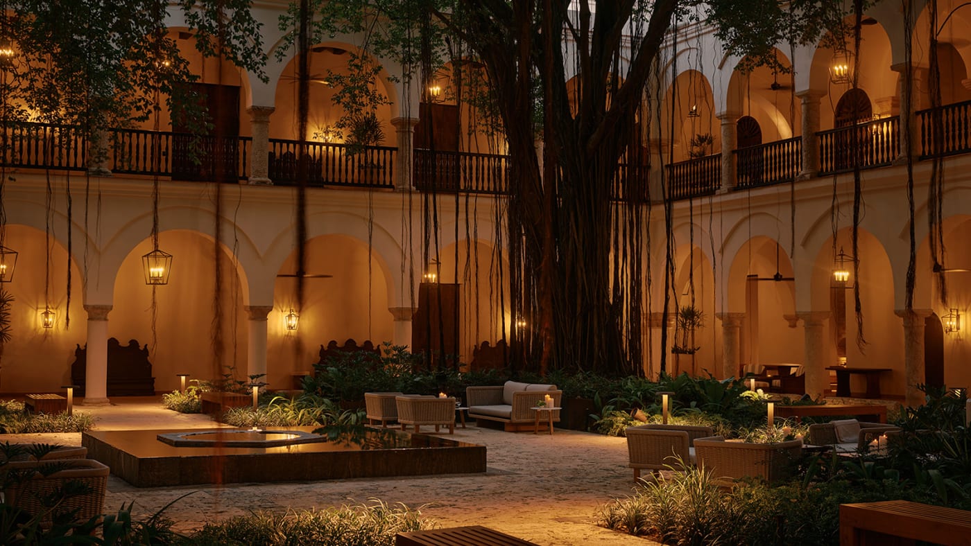 El patio con arcadas del Four Seasons Cartagena de noche, con faroles, salones y un árbol centenario