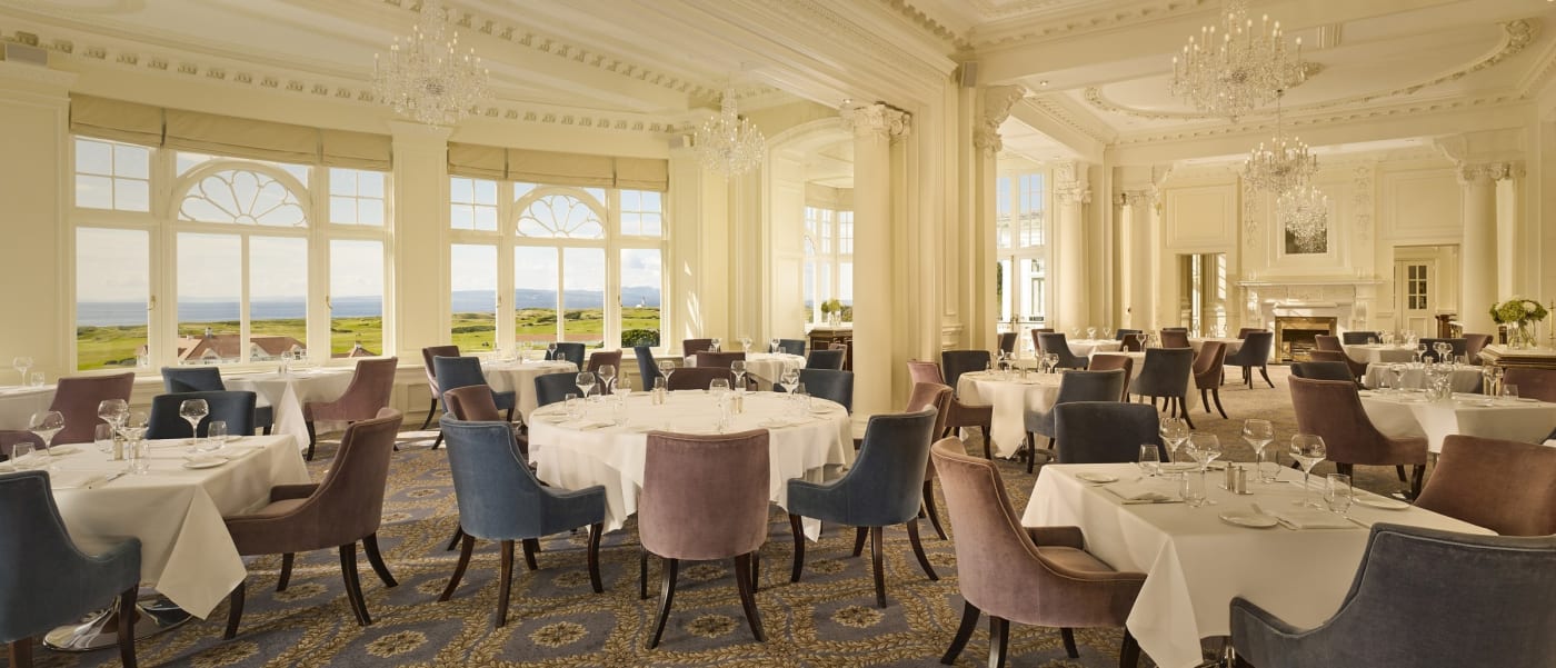 La salle du restaurant 1906 de Trump Turnberry, tables nappées de blanc, lustres et grandes fenêtres ouvertes sur la mer et les links