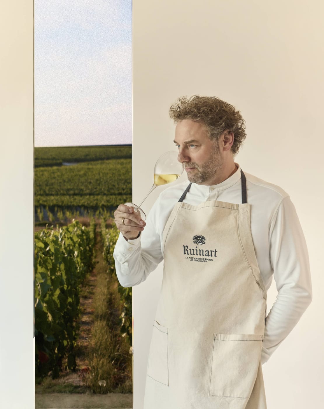 El chef Arnaud Donckele con delantal de Ruinart y una copa de champán en la mano, para La Table Ruinart en Cheval Blanc Paris