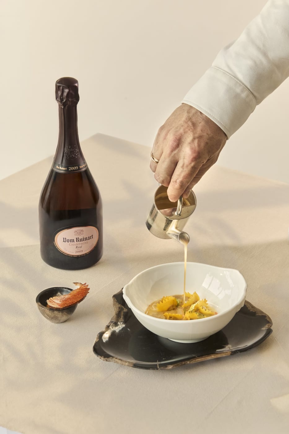 Salsa vertida sobre un plato de Arnaud Donckele junto a una botella de Dom Ruinart Rosé, La Table Ruinart x Cheval Blanc Paris
