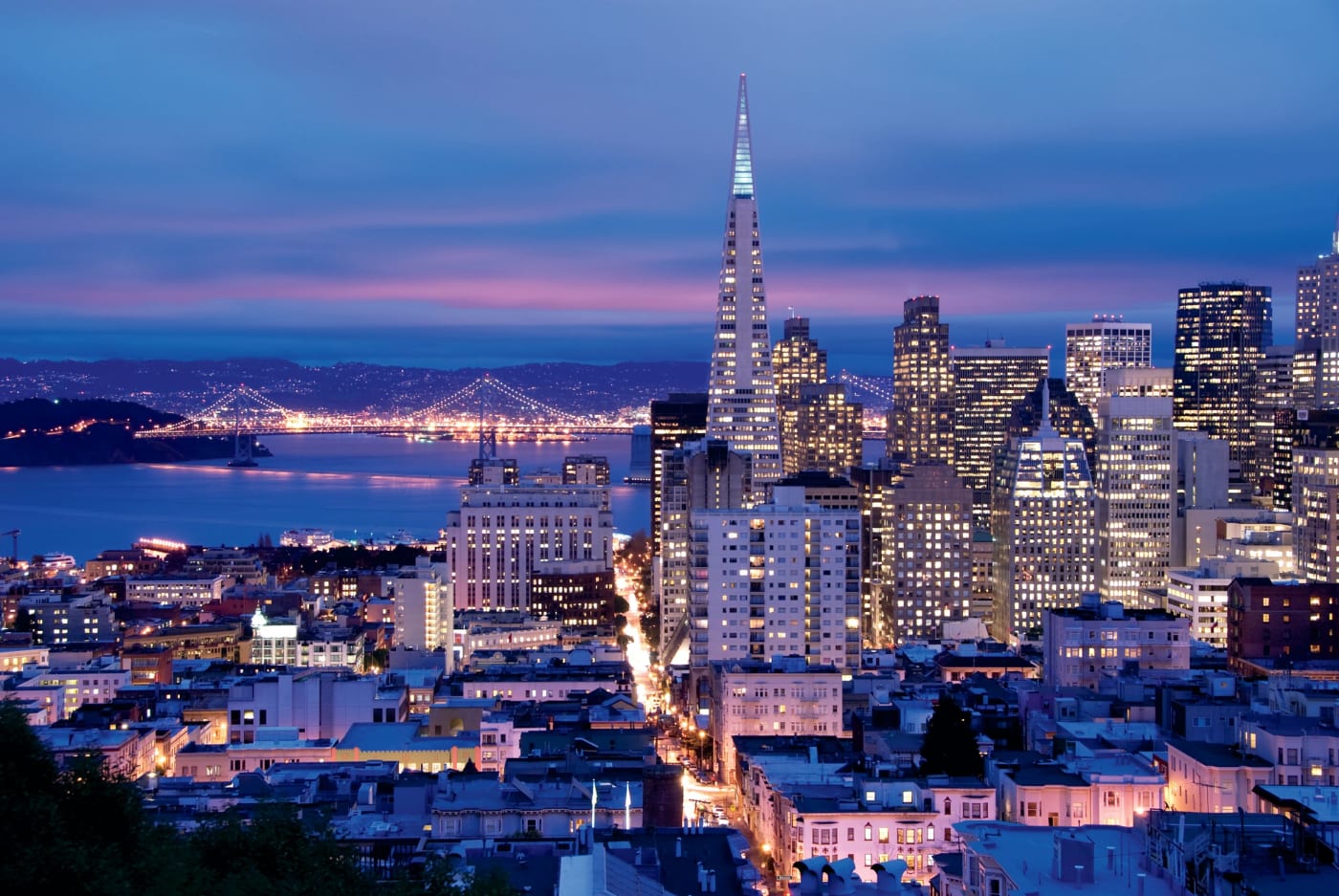 Vista noturna de San Francisco, da Transamerica Pyramid e da Bay Bridge a partir de Nob Hill