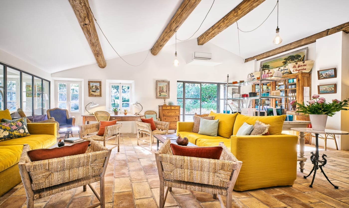 Le grand salon de La Ferme d'Augustin, canapés jaunes, fauteuils en rotin et poutres apparentes