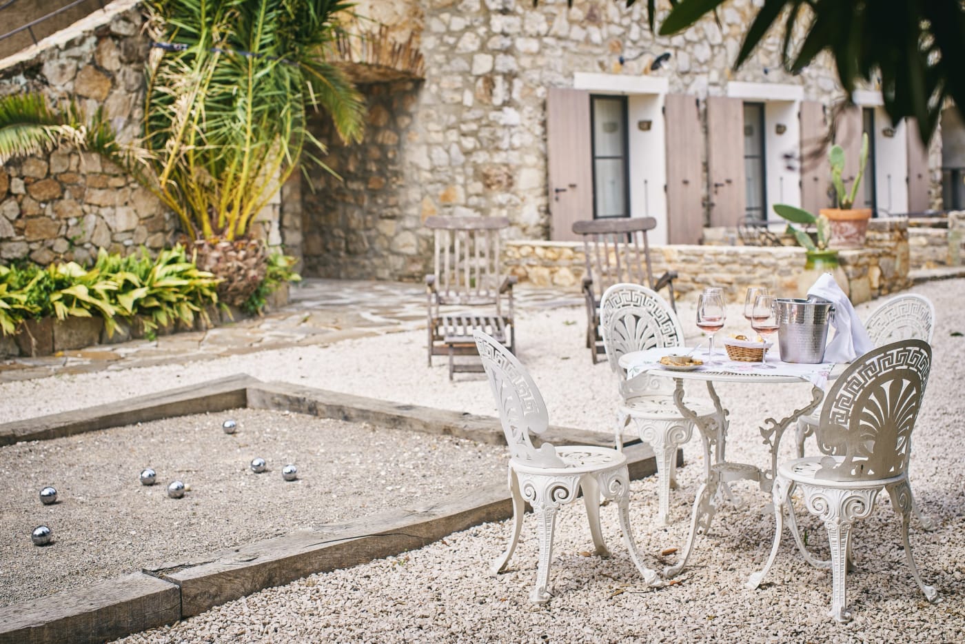La terrasse de La Ferme d'Augustin, mobilier en fer forgé blanc et terrain de pétanque devant la maison en pierre
