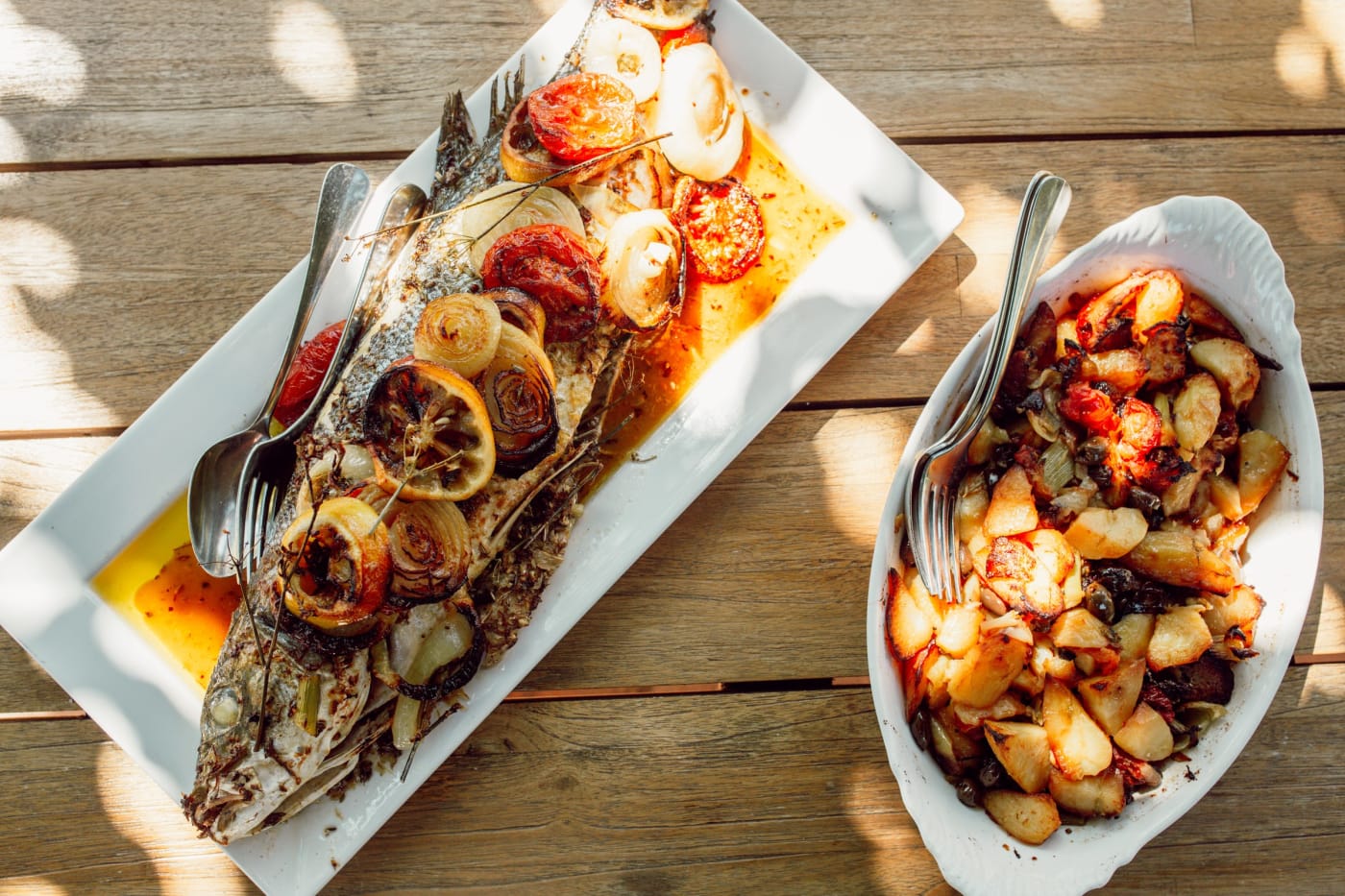Poisson à la provençale cuit au four, au citron et sa garniture, servi sur un plat blanc à La Table d'Augustin