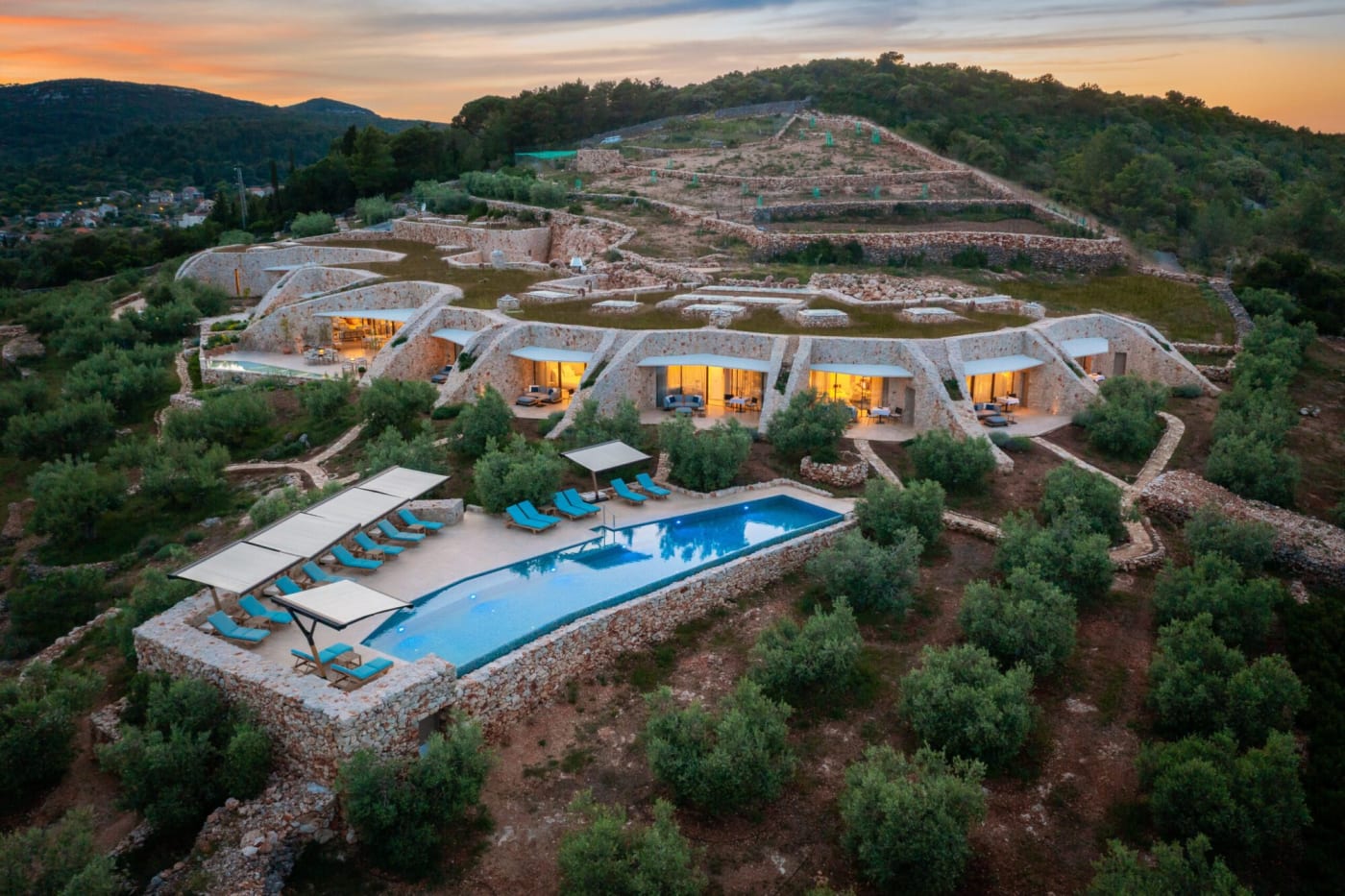 Vue aérienne au crépuscule de l'hôtel Villa Nai 3.3, ses chambres sous toit végétal et sa piscine d'eau de mer à Dugi Otok