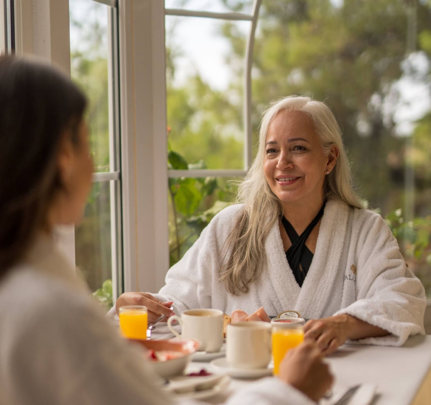 Dos huéspedes en albornoz comparten un desayuno junto a una ventana en Palasiet