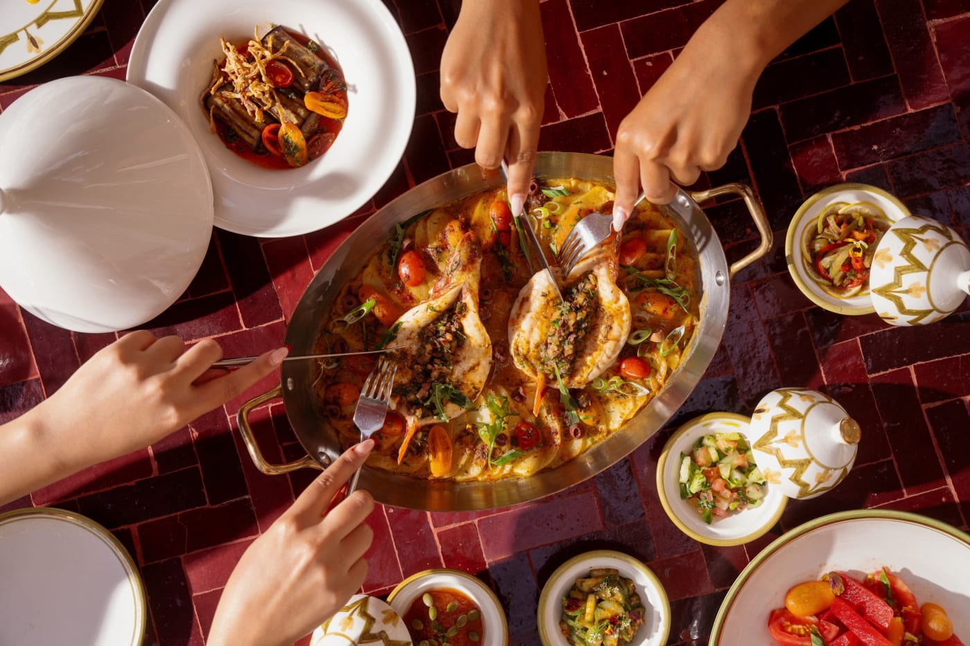 Convives partageant un plat et des salades marocaines sur une table en zellige rouge chez Inara, au Four Seasons Resort Marrakech
