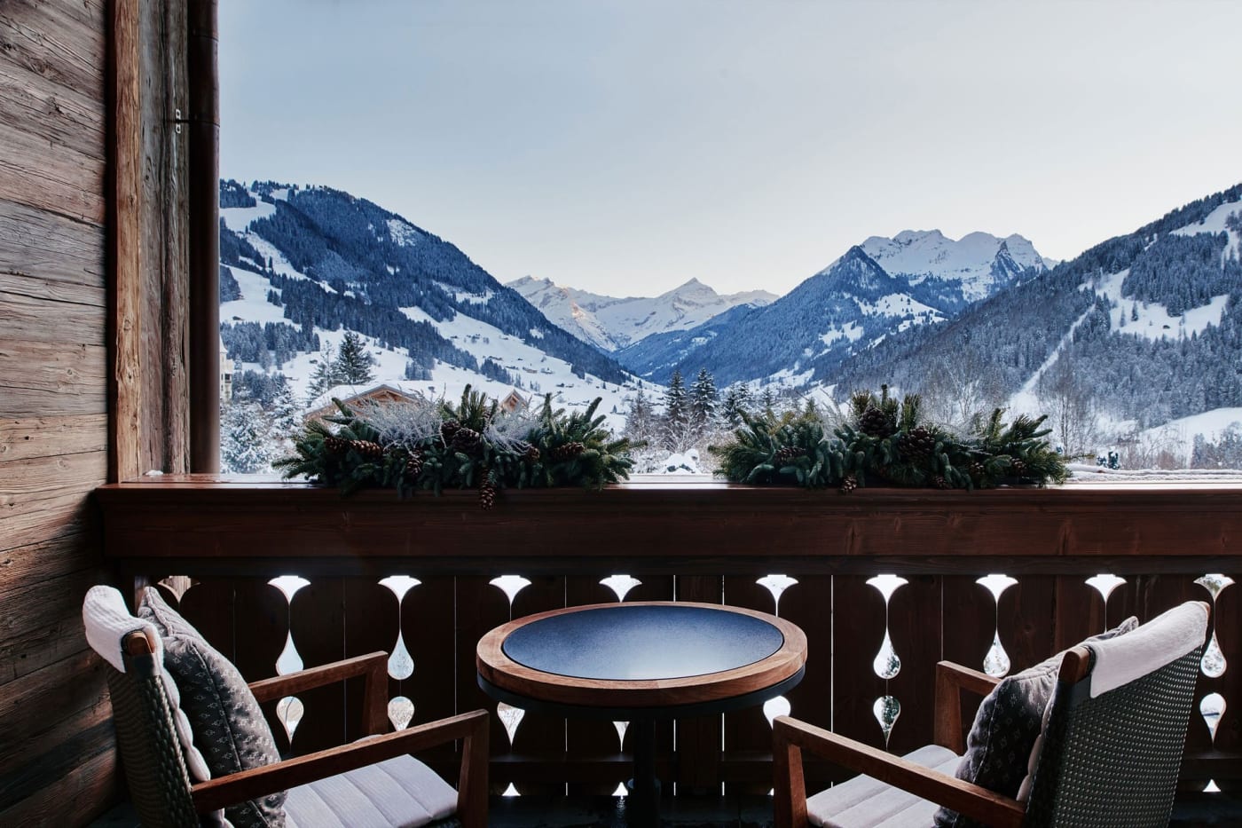 La terrasse privée d'une chambre de The Alpina Gstaad, fauteuils et table face aux montagnes enneigées du Saanenland