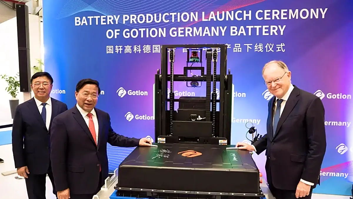 Tres hombres en traje posan junto a un gran paquete de baterías con firmas en su tapa, frente a un cartel azul que dice «BATTERY PRODUCTION LAUNCH CEREMONY OF GOTION GERMANY BATTERY».