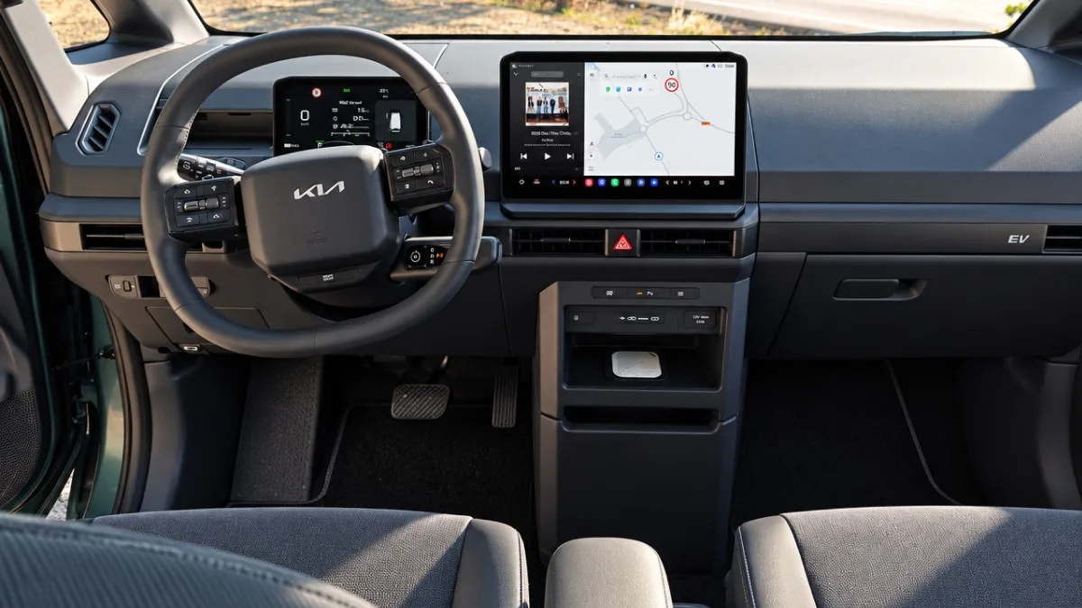Vista frontal del salpicadero del interior de un coche Kia, mostrando el volante multifunción, el cuadro de instrumentos digital y una pantalla central táctil encendida con navegador y reproductor multimedia.